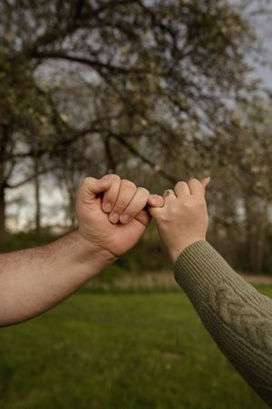 Two hands reaching out to pinky promise against a natural backdrop.