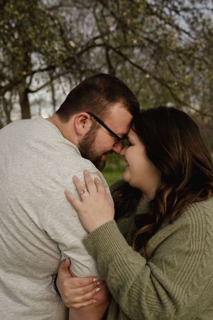 A tender embrace between a couple wearing casual sweaters in a park setting.