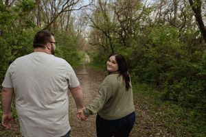 A couple walking hand in hand along a wooded nature trail.