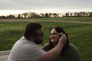 Two people share a romantic kiss in a green field at sunset.