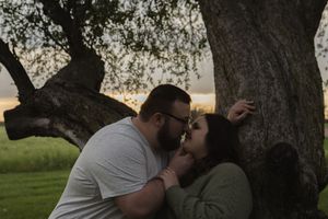 Two people share a romantic kiss under the branches of a large tree.