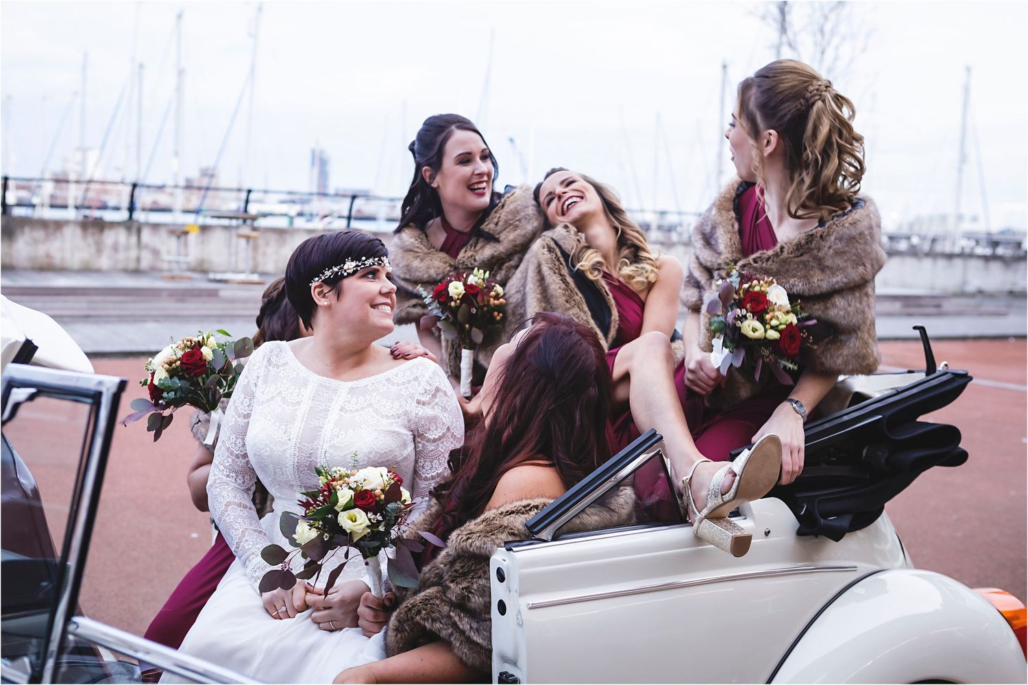Four people sit together and laugh while wearing formal dresses in light blue and white in an outdoor garden setting.