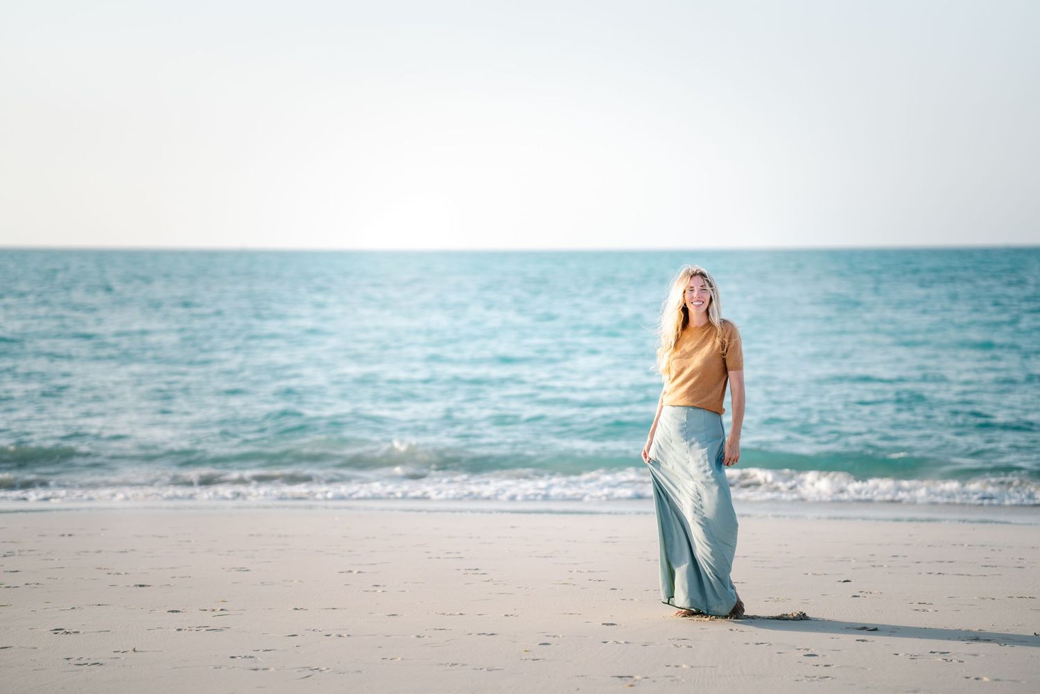 Person in yellow sweater standing alone on serene beach at sunset.