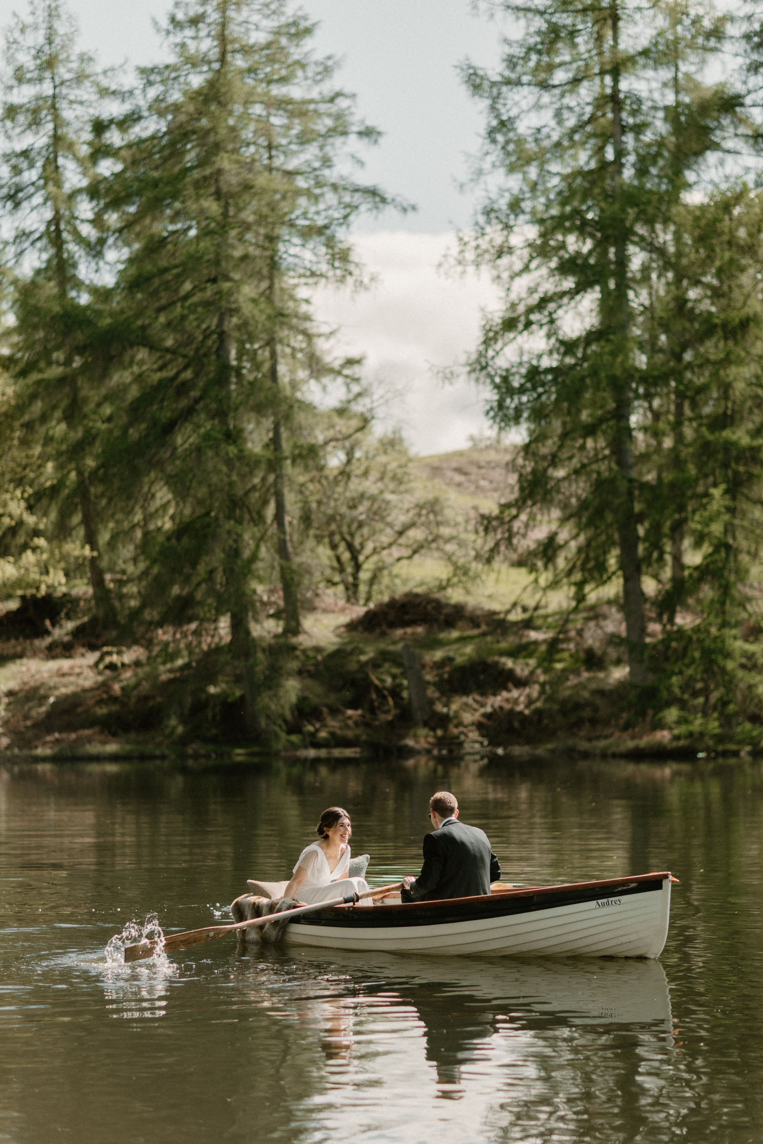 A couple enjoys a peaceful canoe ride surrounded by tall evergreen trees along a serene lake.