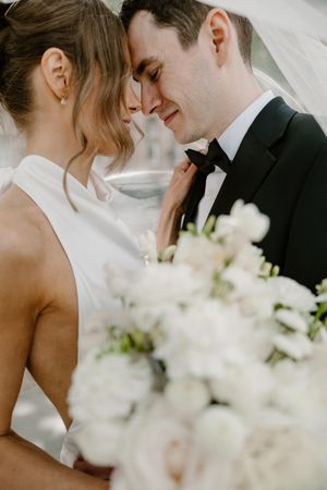 Romantic wedding couple shares intimate moments with delicate white floral arrangements in the foreground.