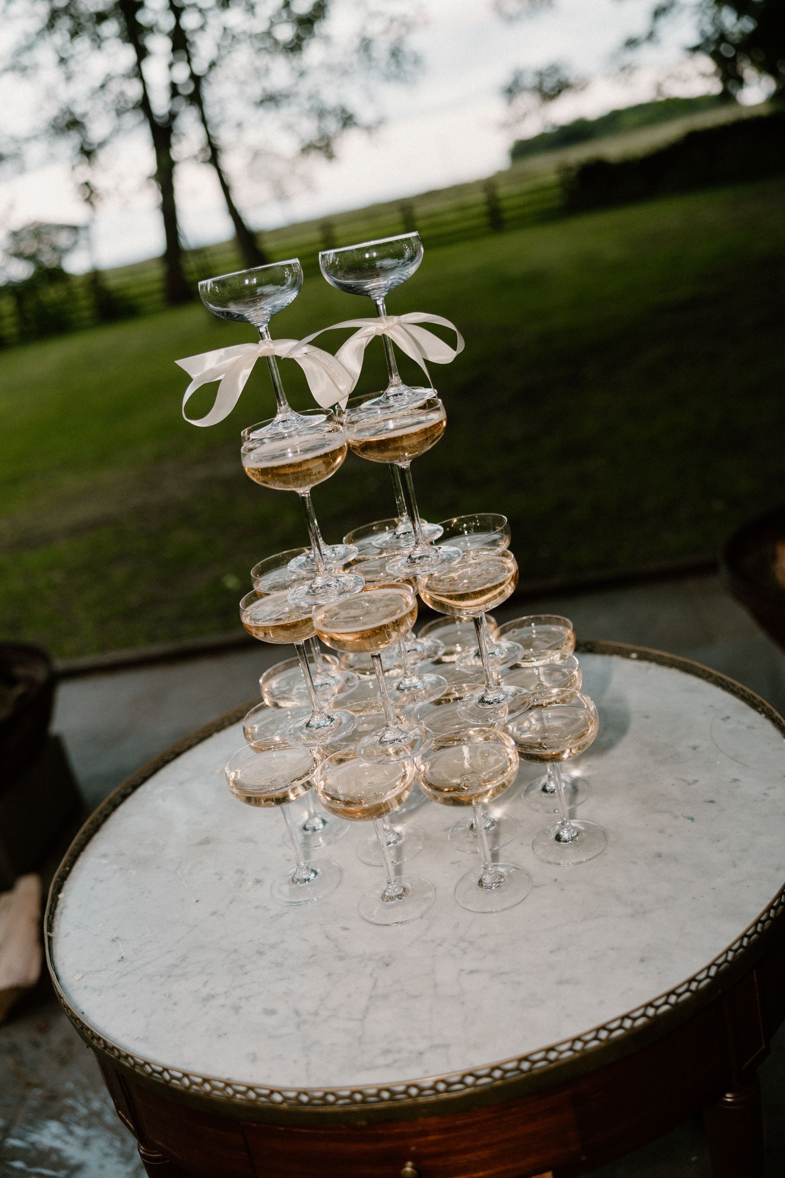 Vintage champagne coupe glasses elegantly stacked in a pyramid formation on a rustic table for a wedding celebration.