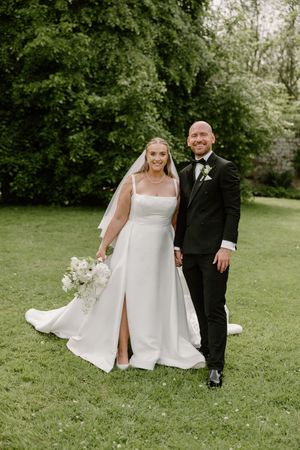 A couple in wedding attire walks together on a grassy lawn showing dynamic movement of the bride's flowing white dress.