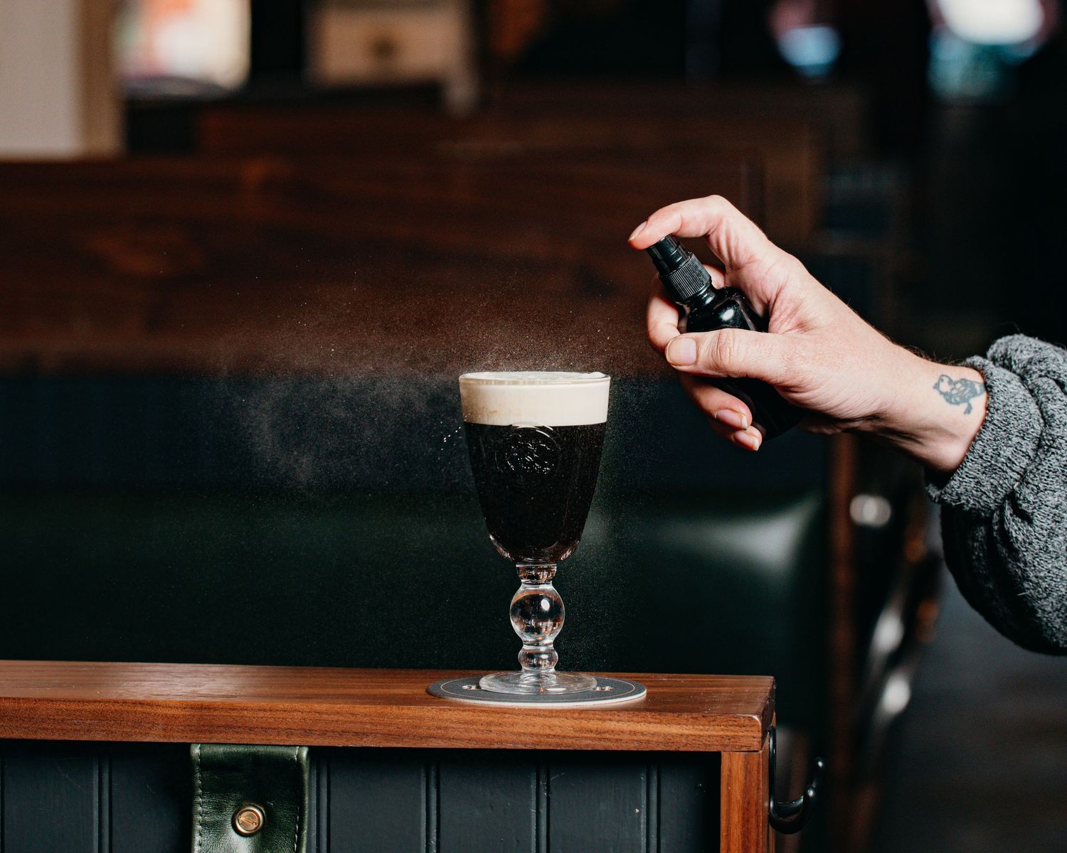 Hand sprinkling garnish on dark beer with creamy foam head in stemmed glass.