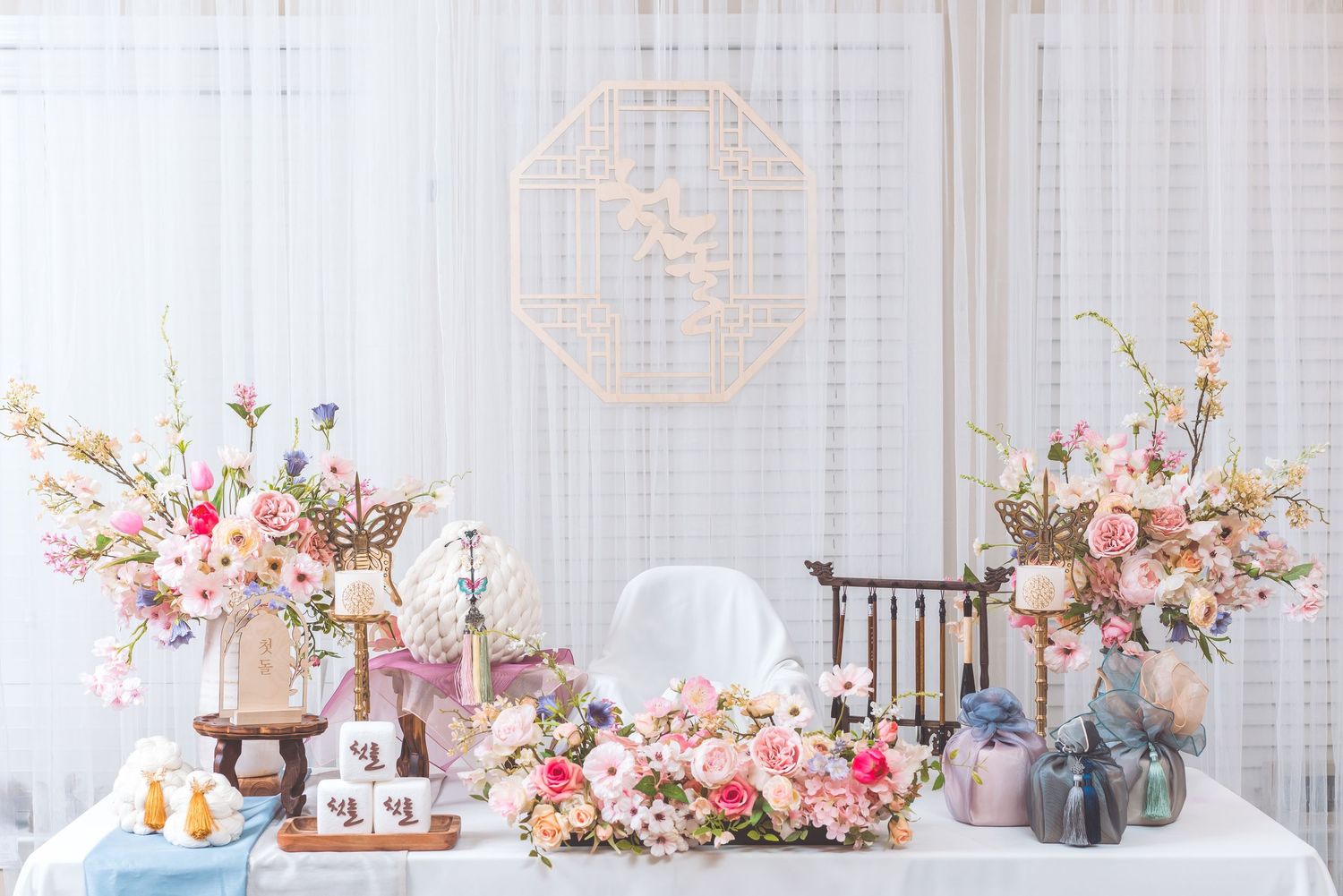 An elegant party setup with white backdrop featuring floral arrangements, desserts, and decorative elements.