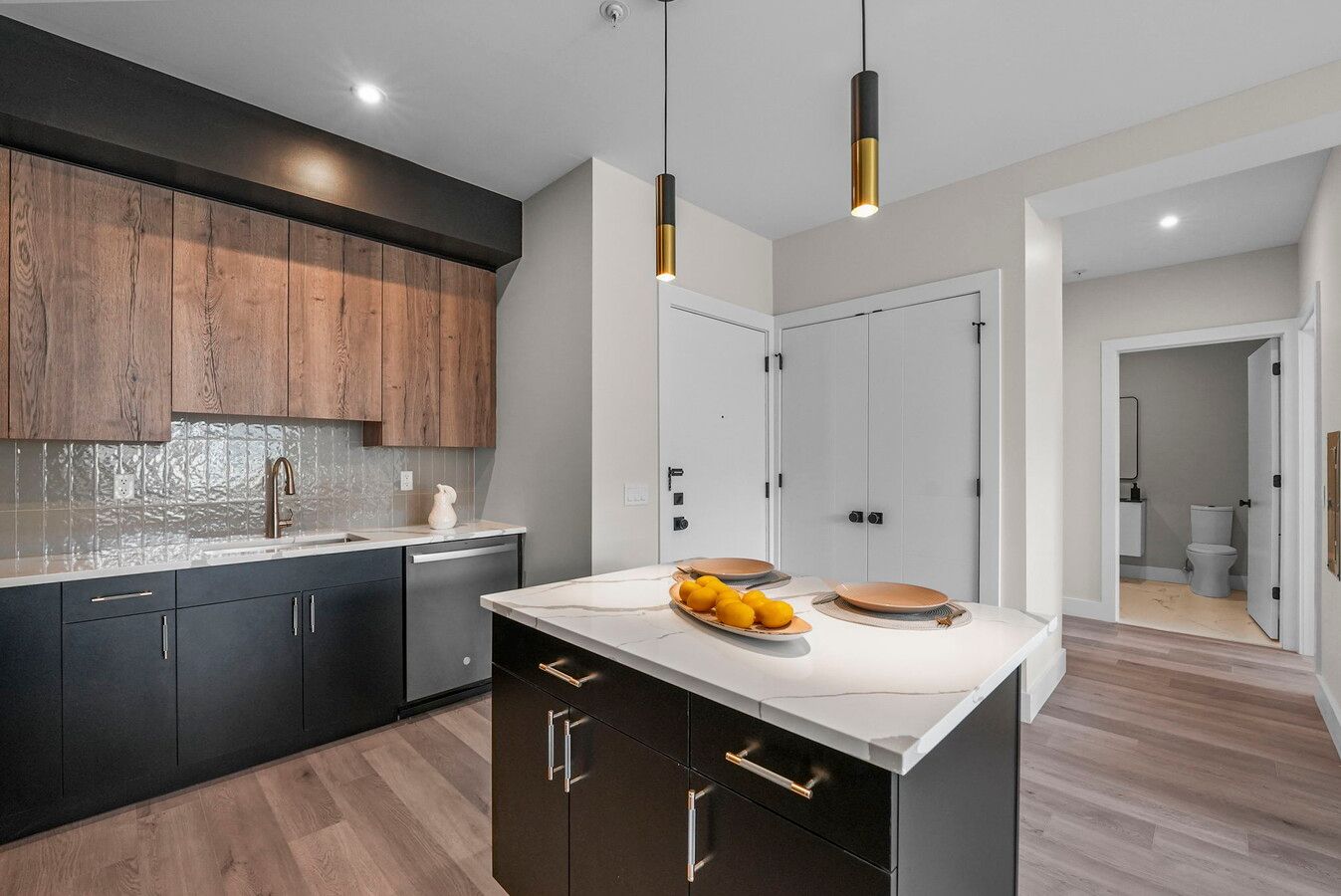 Modern kitchen interior with two-tone cabinets featuring dark base and wood upper cabinets, white island and pendant lights.