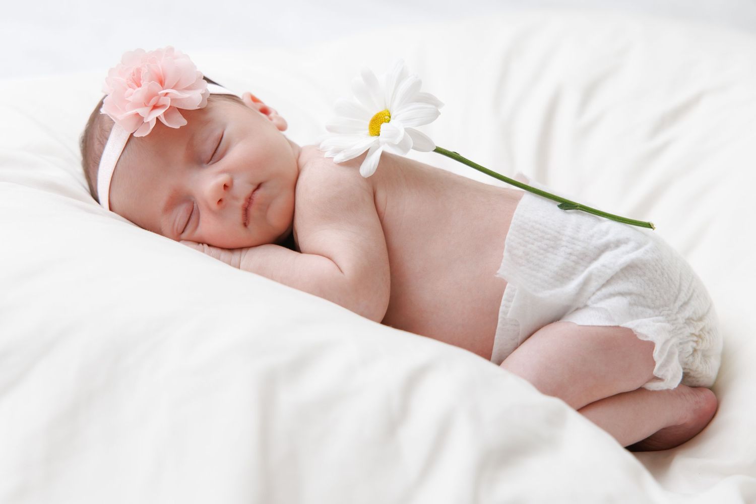 Peaceful newborn photography with white bedding and delicate daisy flower accents.
