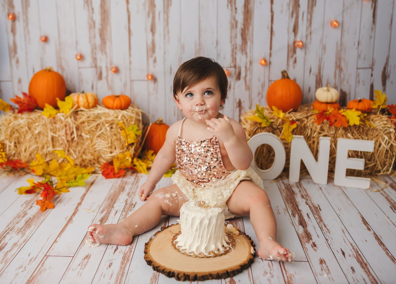 Charlottesville baby photographer captures fall cake smash with one-year-old girl in sequin romper and festive autumn decor.