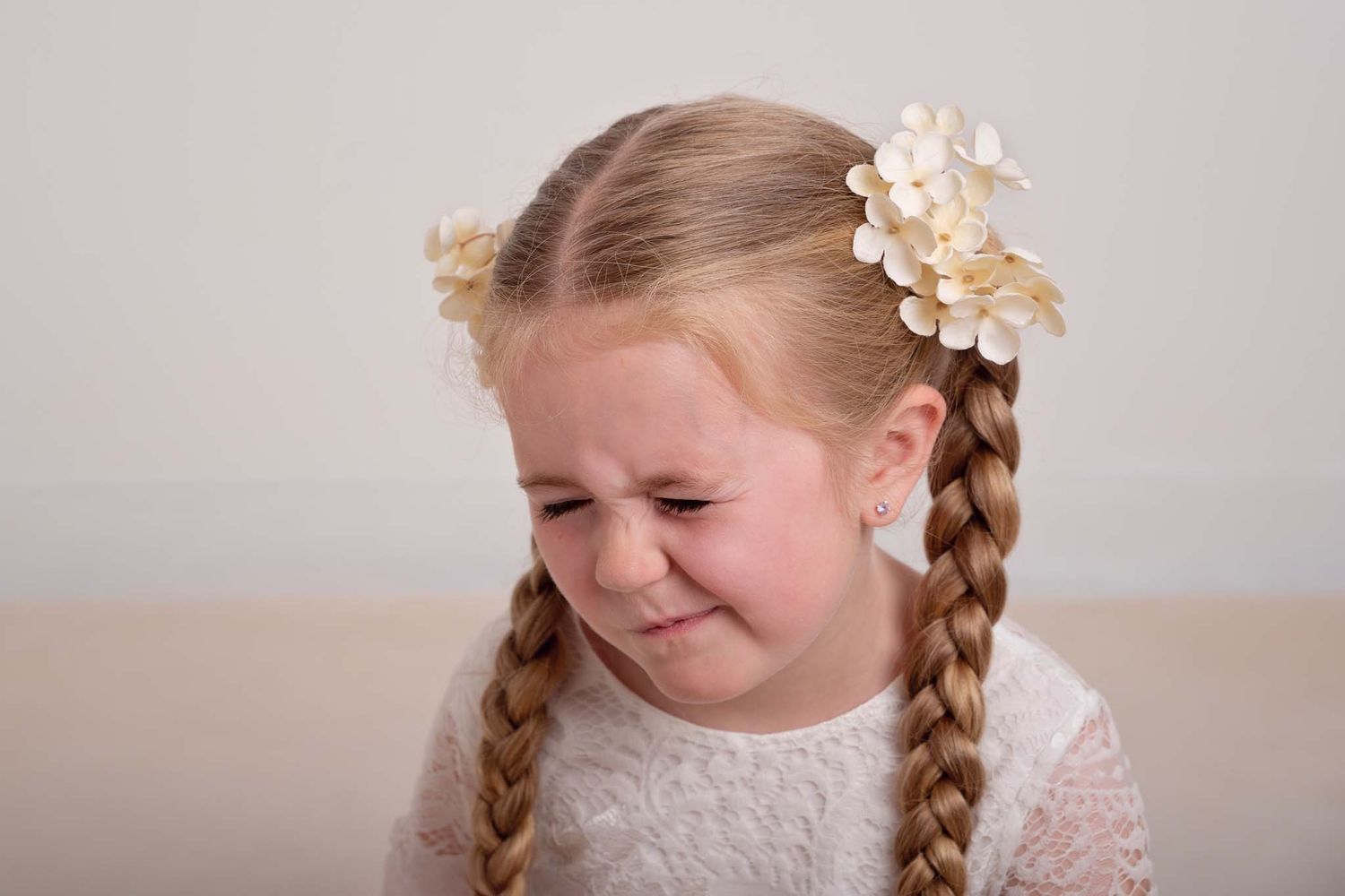 Five-year-old girl with long braids and floral hair clips scrunches her face in a playful expression during a sibling newborn photo session.