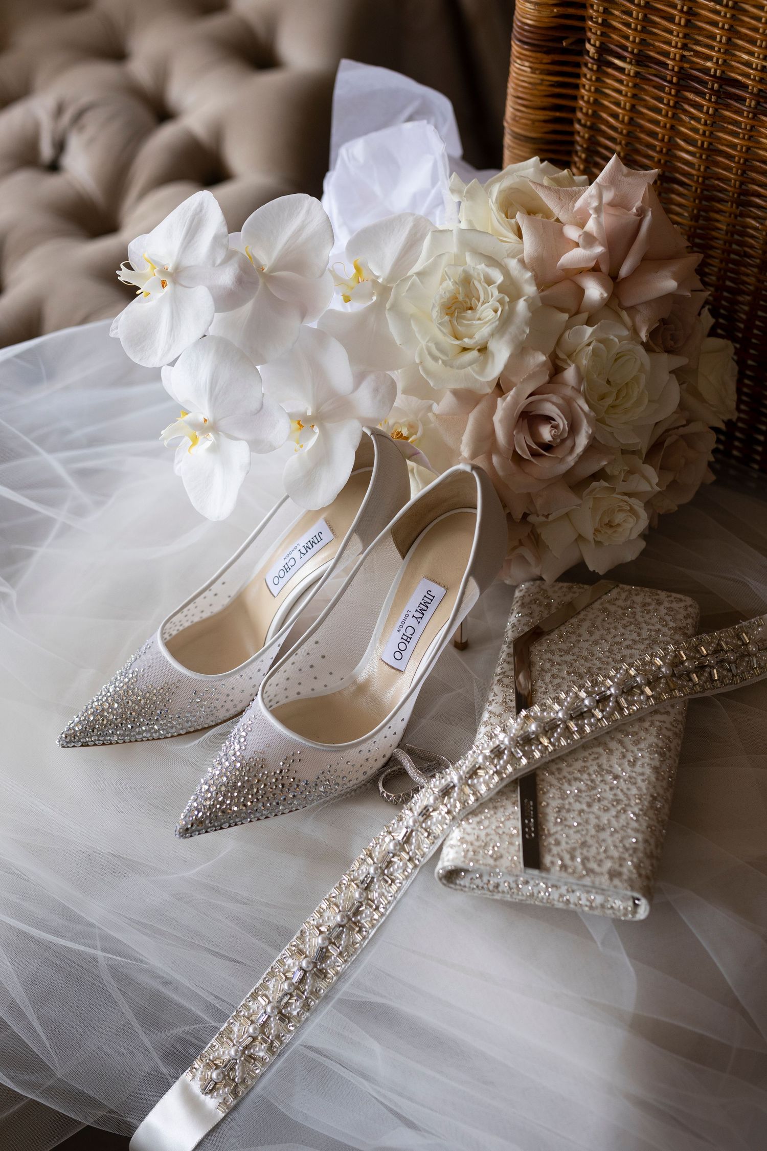 Elegant bridal accessories featuring sparkly Jimmy Choo heels, white orchids, roses, and crystal-embellished accessories on tulle.