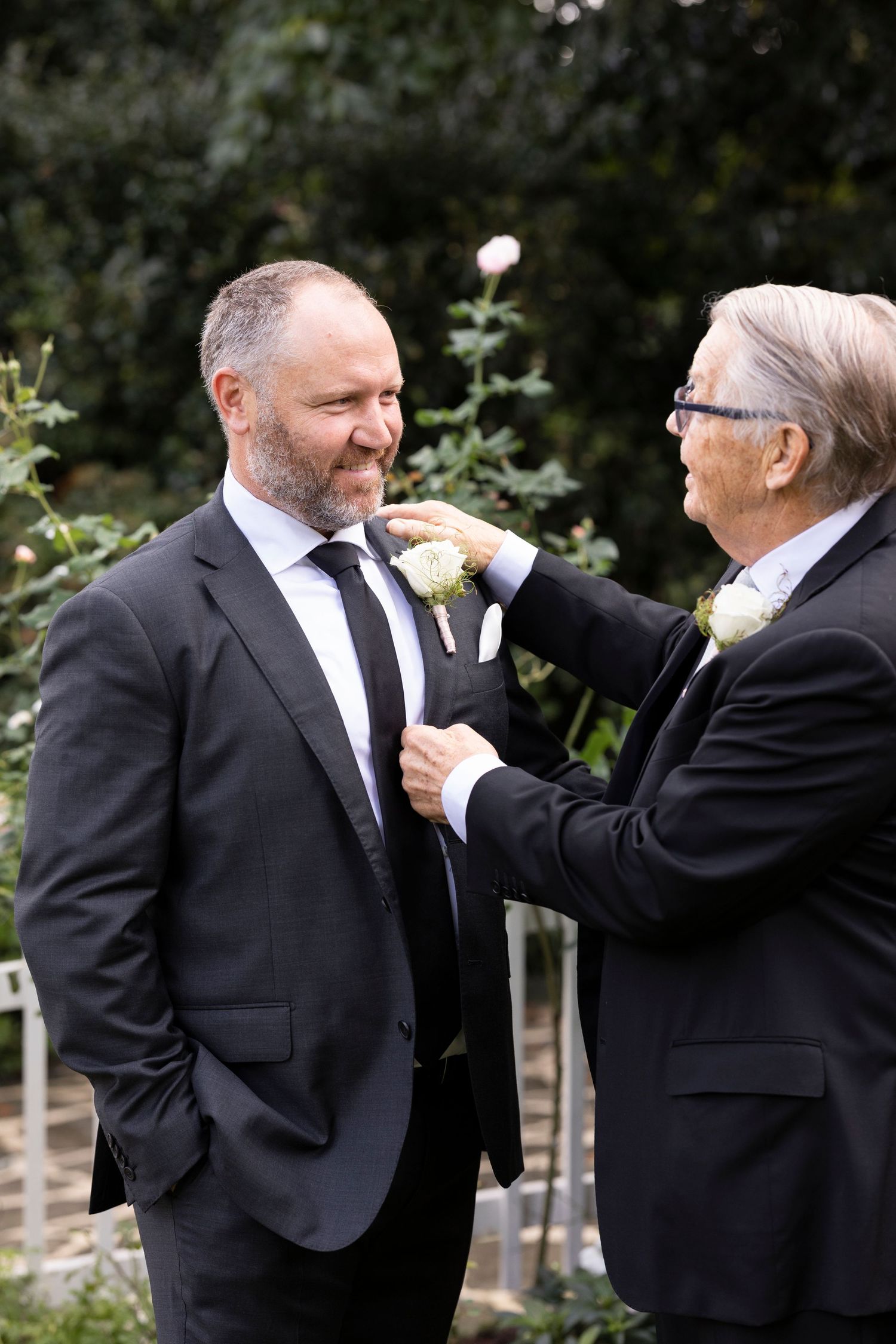 Two people in black suits and ties adjusting each others' boutonnieres in a series of candid wedding photos.