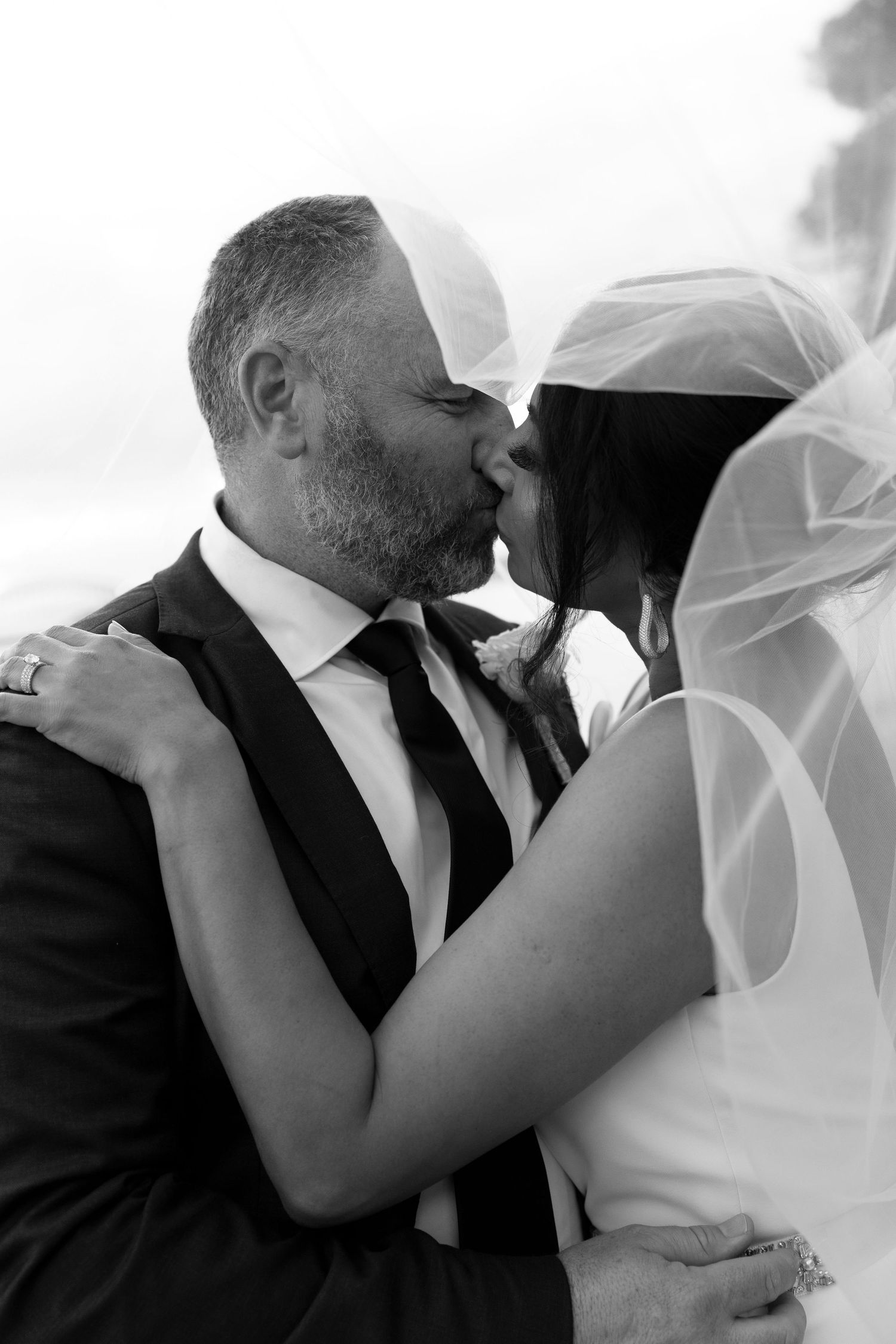 A tender moment between newlyweds sharing an intimate kiss, captured in elegant black and white photography.