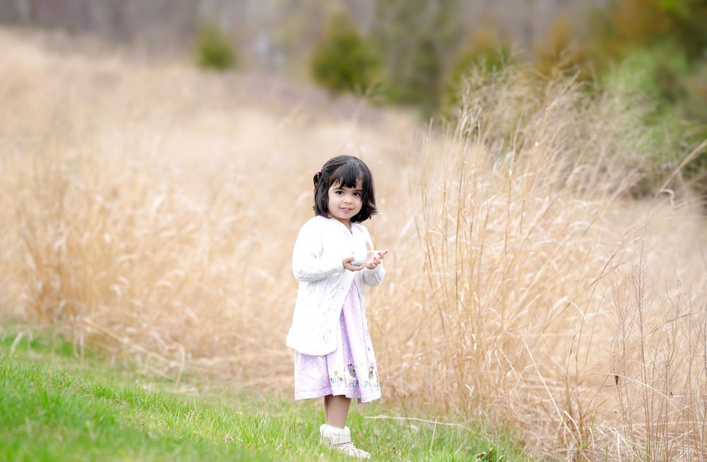 A child in white dress standing in tall golden grass field during golden hour.