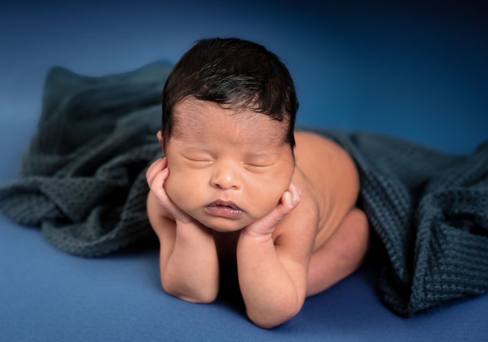 A peaceful sleeping newborn baby wrapped in cozy gray blankets against a dark blue background.