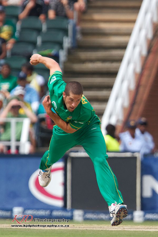 Cricket bowler in bright green uniform follows through on delivery motion during match play.
