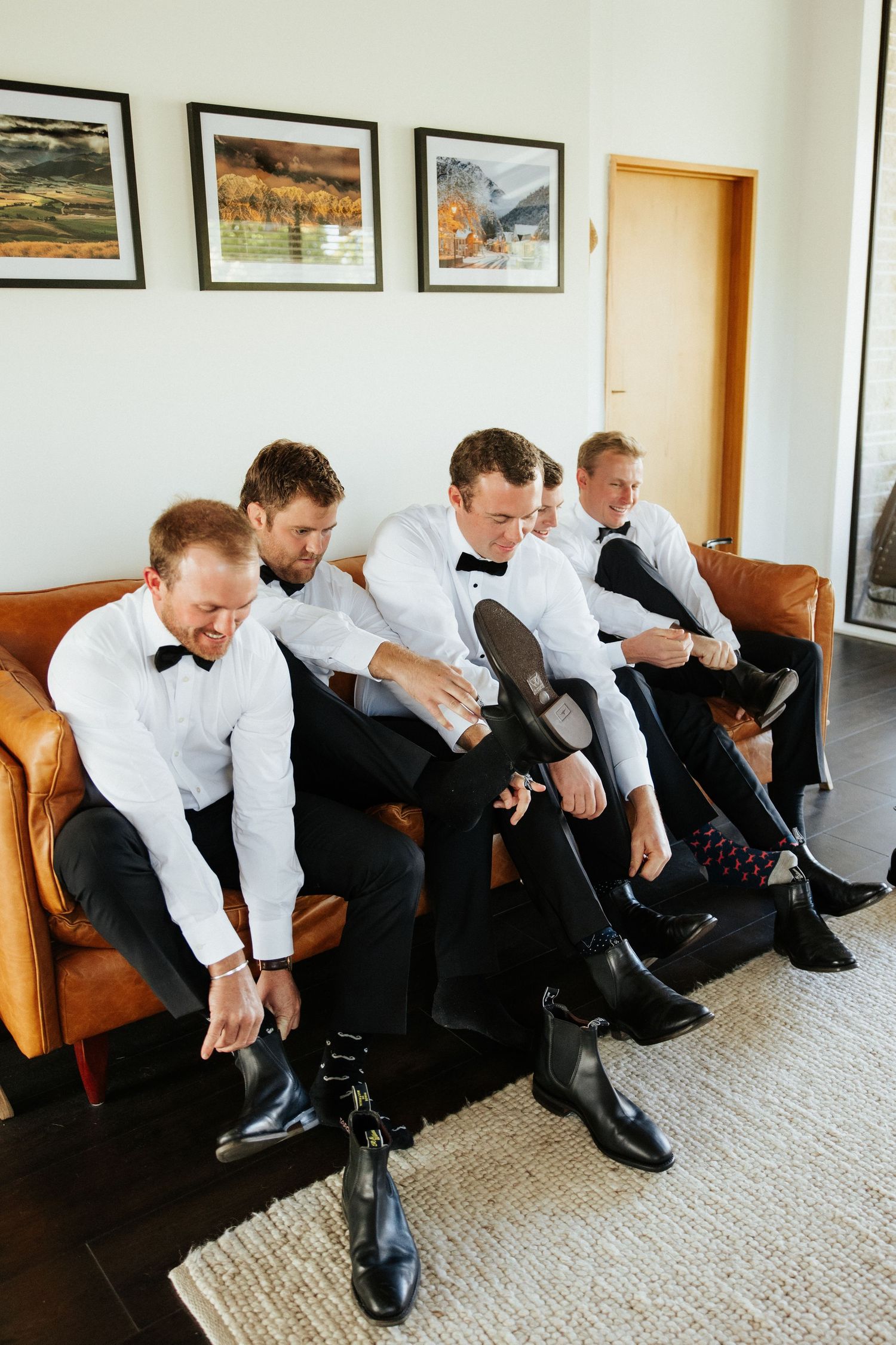 Multiple people in formal black pants and white shirts sit on a couch putting on dress shoes in a sequence.