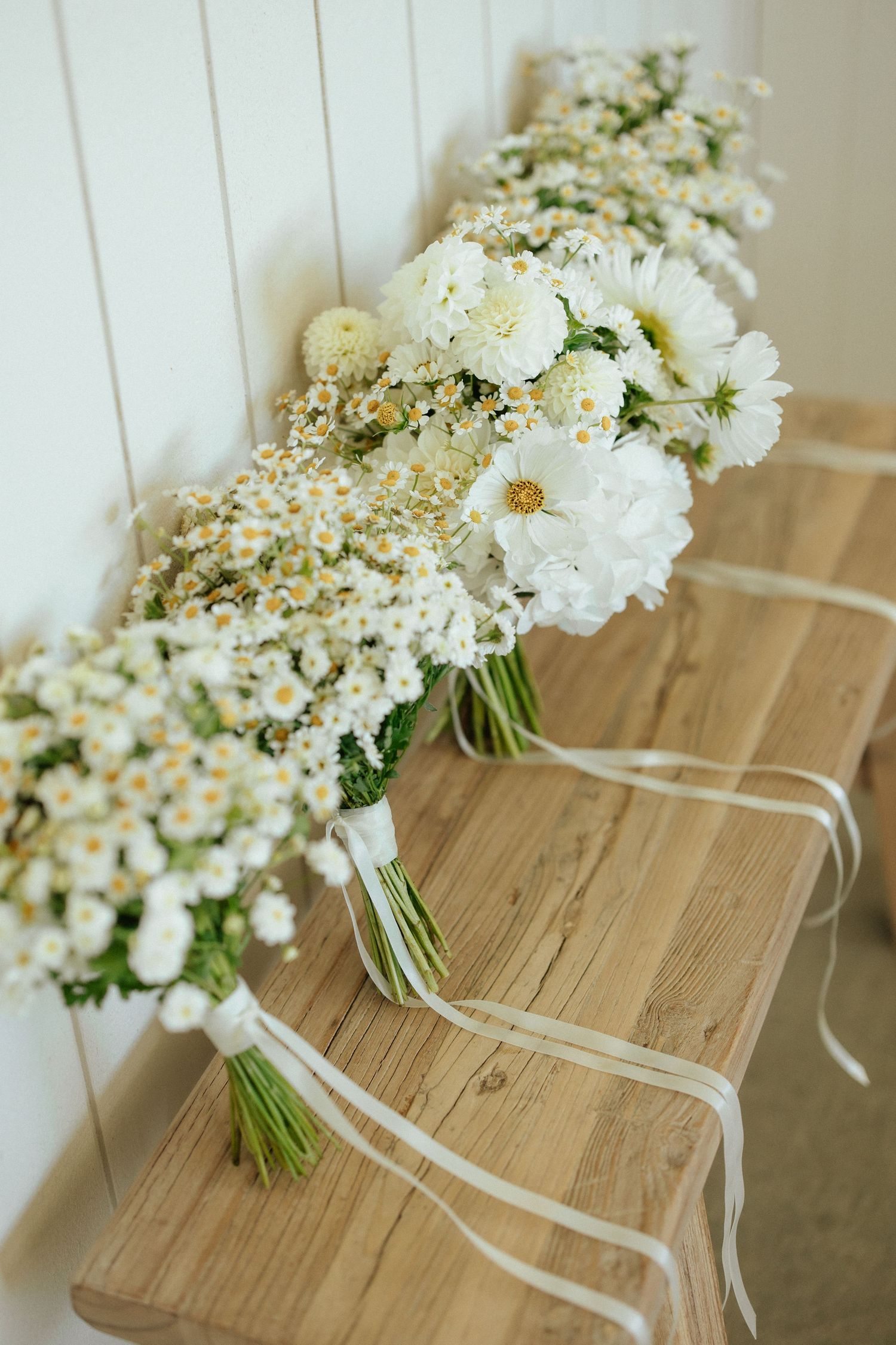 White floral bouquets with daisies and baby's breath tied with ribbons rest on a wooden surface.