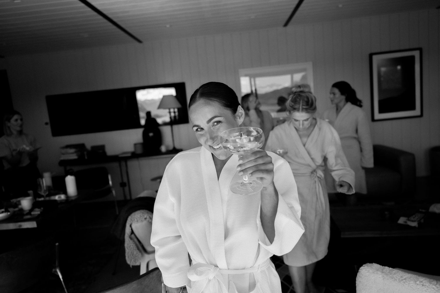 A person in a white robe smiles while holding a glass in a black and white photograph.