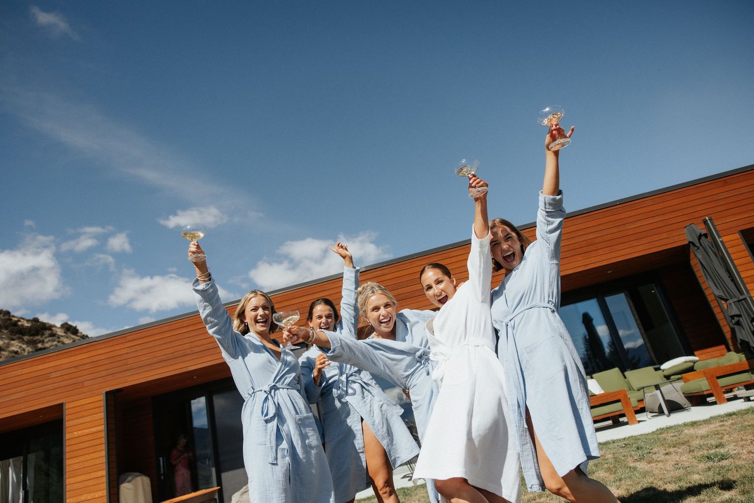 A group of people in light blue outfits jumping and celebrating joyfully outside a modern wooden building.