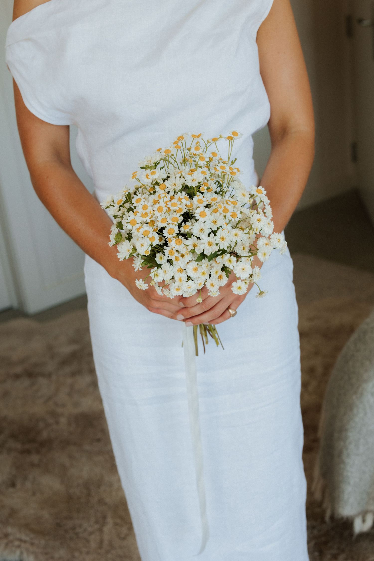 A delicate bouquet of white daisies held against a flowing white wedding dress.