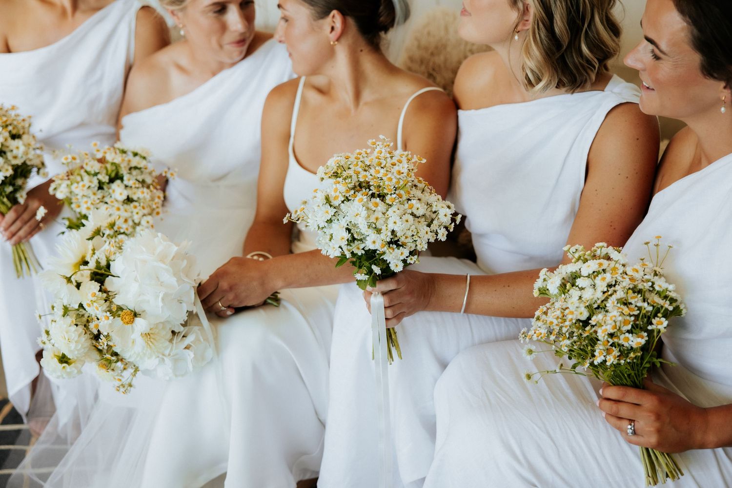 Row of bridesmaids in white dresses holding delicate bouquets of white and green flowers.