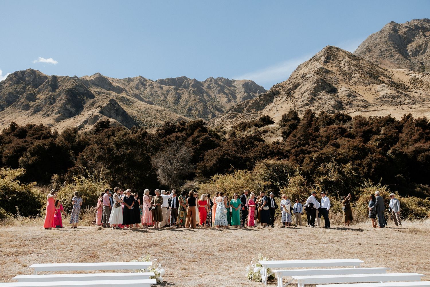 Wedding guests gathered on a hill overlooking majestic mountain peaks during an outdoor ceremony.