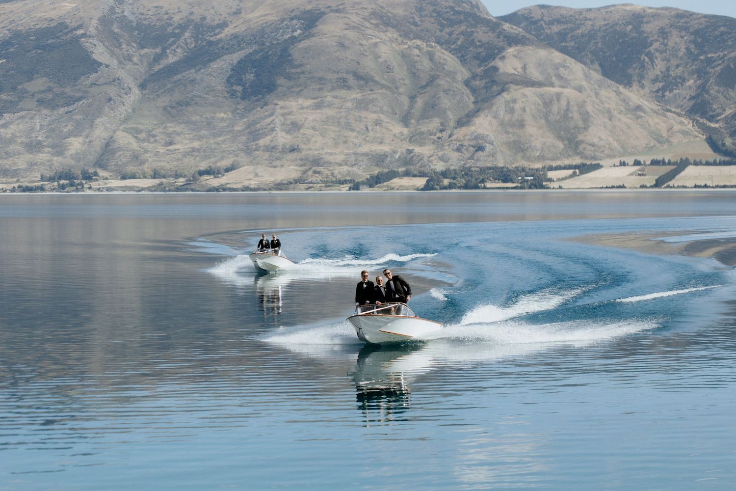 Two speed boats create dramatic wakes while racing across a scenic mountain lake.