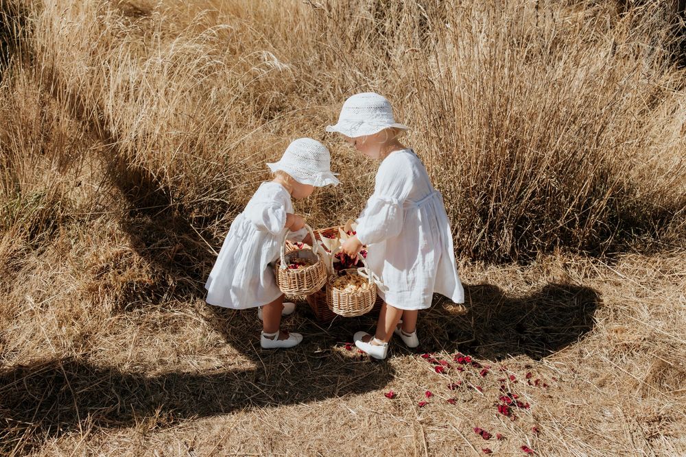 Two children in white dresses playing together in a sunlit field of tall grass.