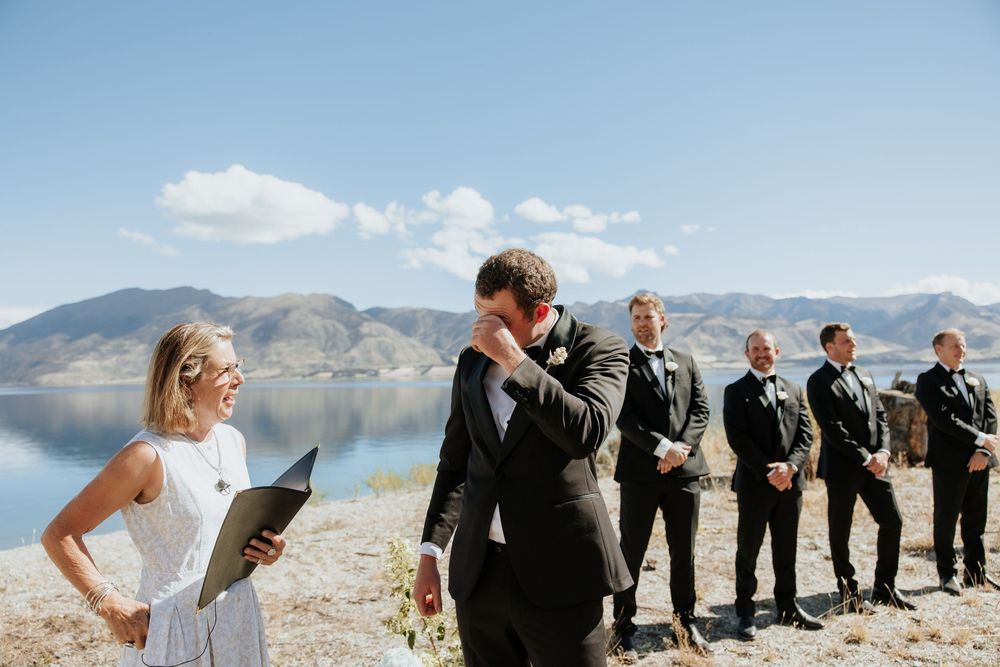 Wedding party lined up against dramatic mountain landscape and blue sky on sunny day.