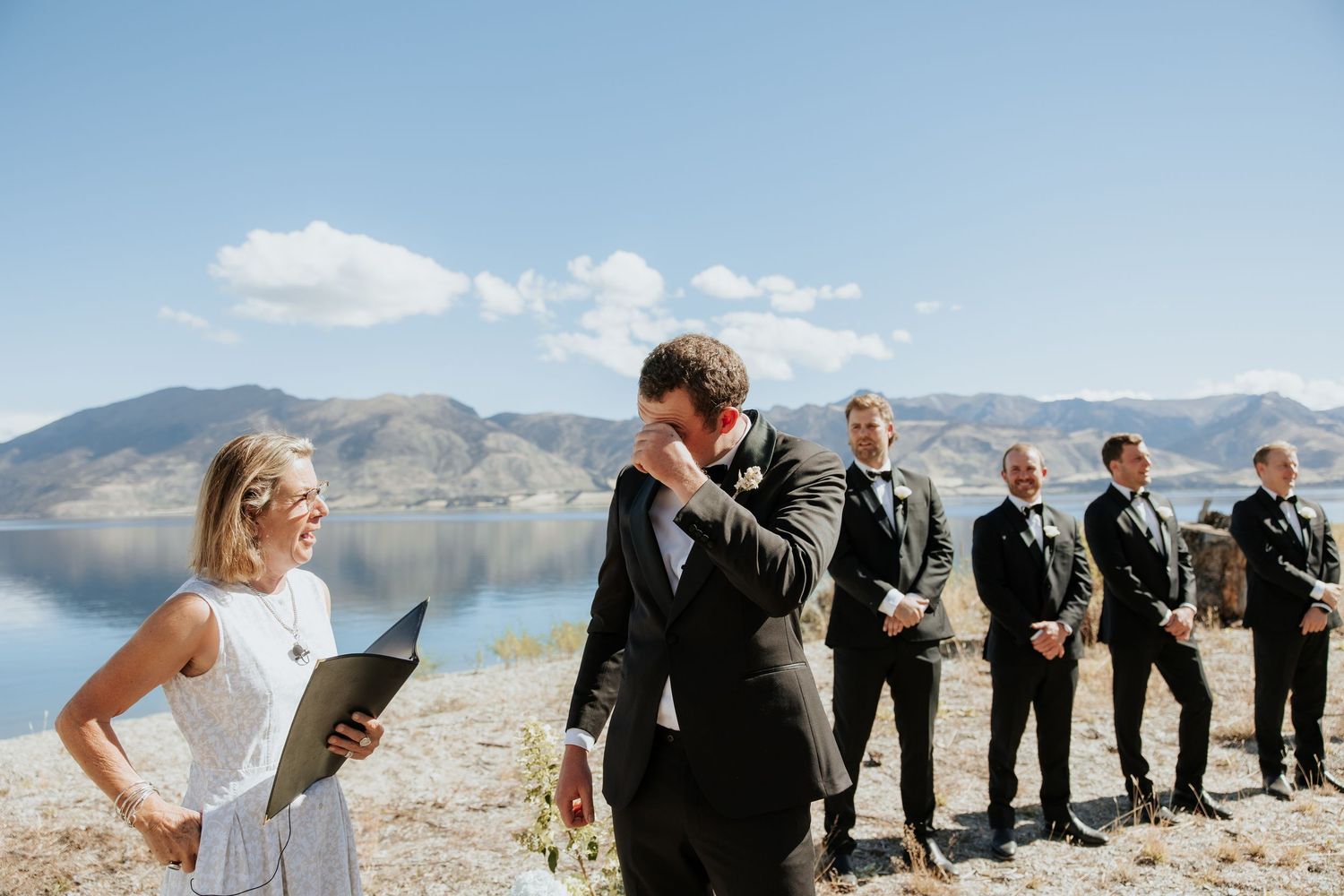 Wedding party lined up against dramatic mountain landscape and blue sky on sunny day.
