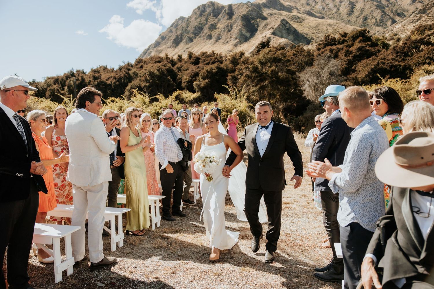 A wedding ceremony taking place outdoors with mountains in the background on a sunny day.