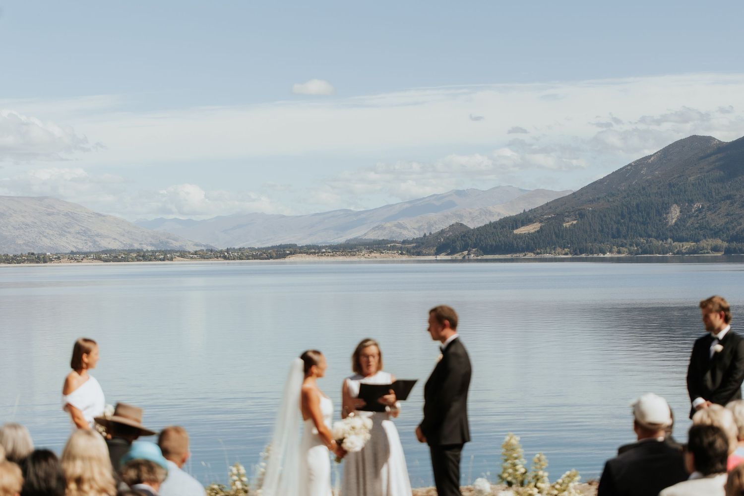An intimate lake shore wedding ceremony with mountains and calm waters creating a scenic backdrop.