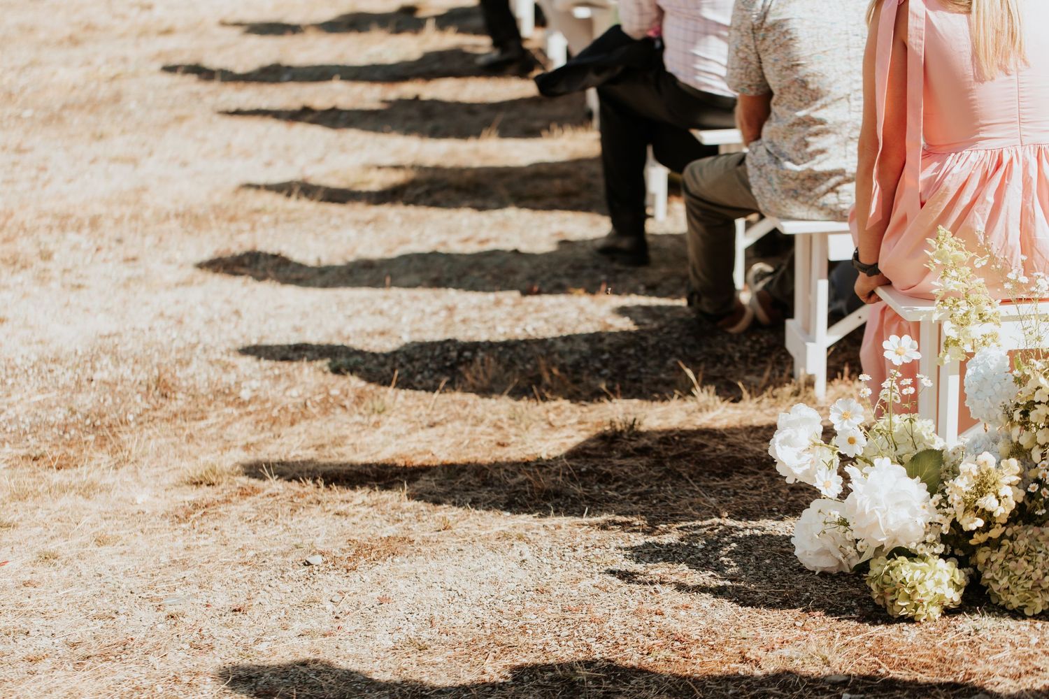 White floral wedding decorations line an outdoor ceremony aisle against a sunny desert landscape.