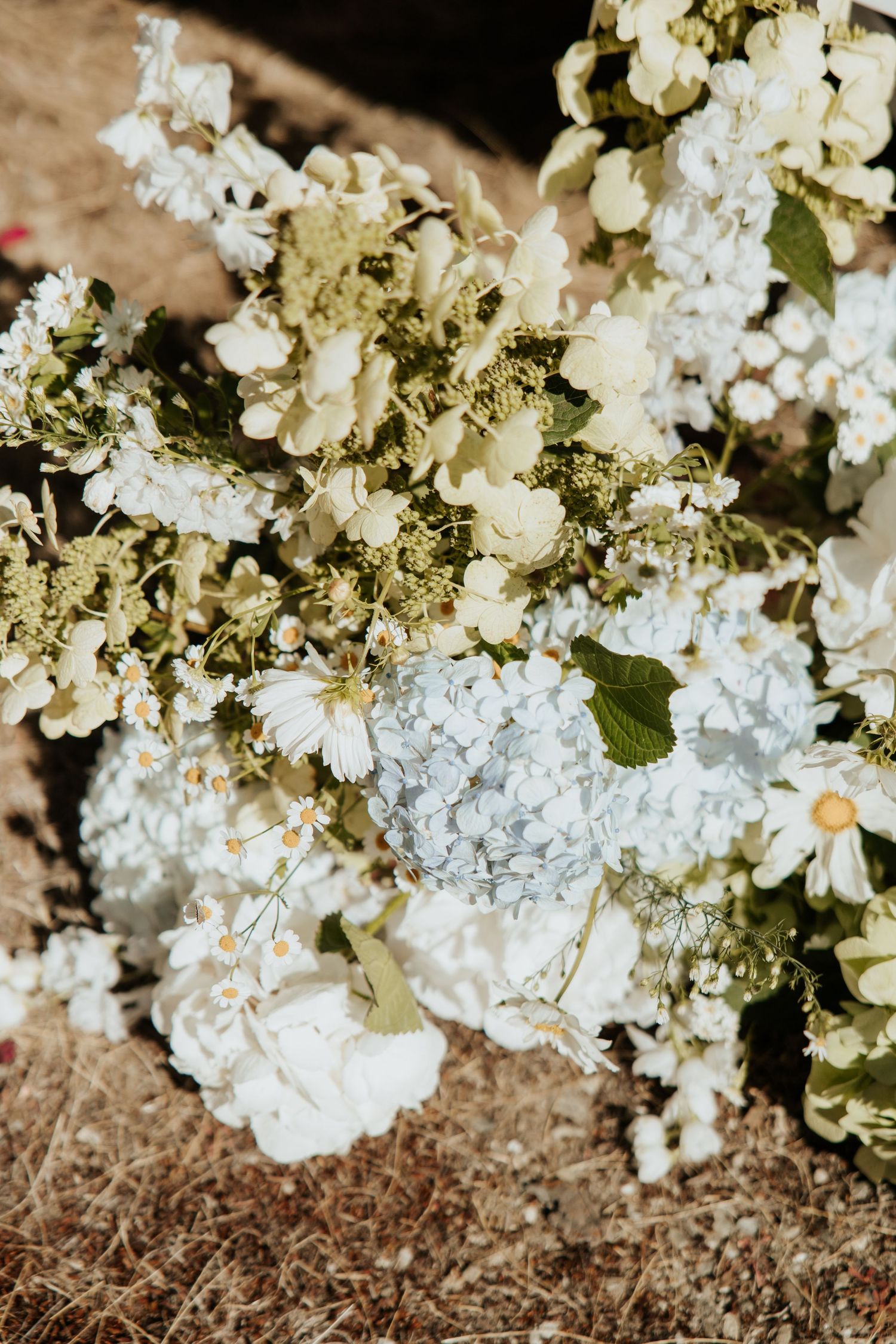 Close-up of white hydrangea and delicate floral arrangements with soft green accents against a natural background.