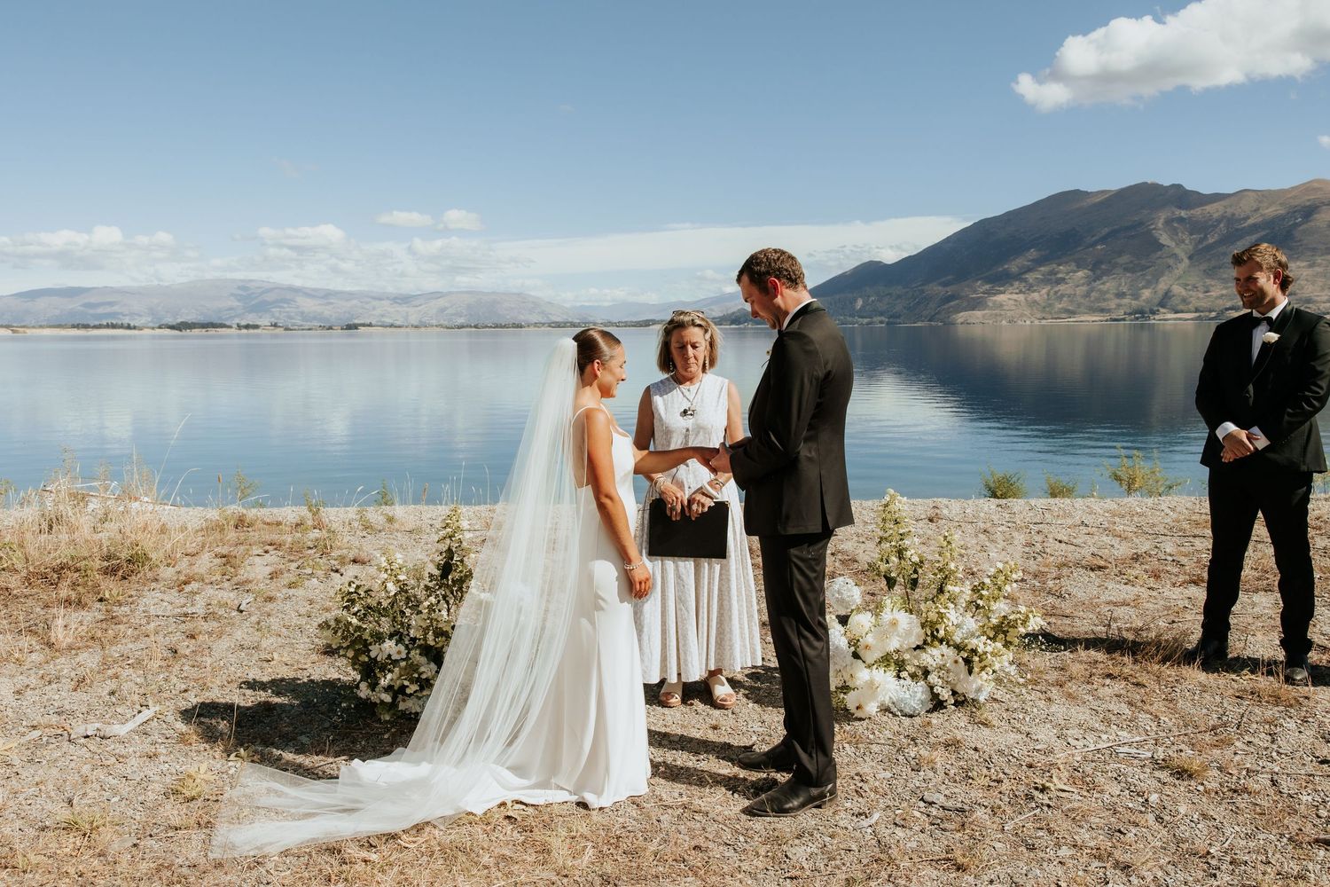 Scenic lakeside wedding ceremony with mountains and blue sky in the background.