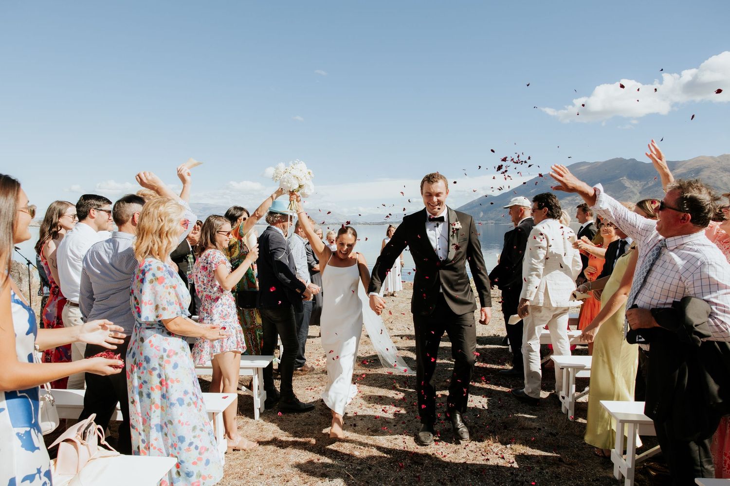 Wedding guests celebrate outdoors with raised arms against a beautiful mountain backdrop.