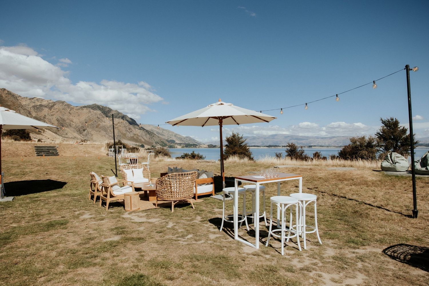 Rustic outdoor wedding venue setup with string lights and white seating overlooking mountains.