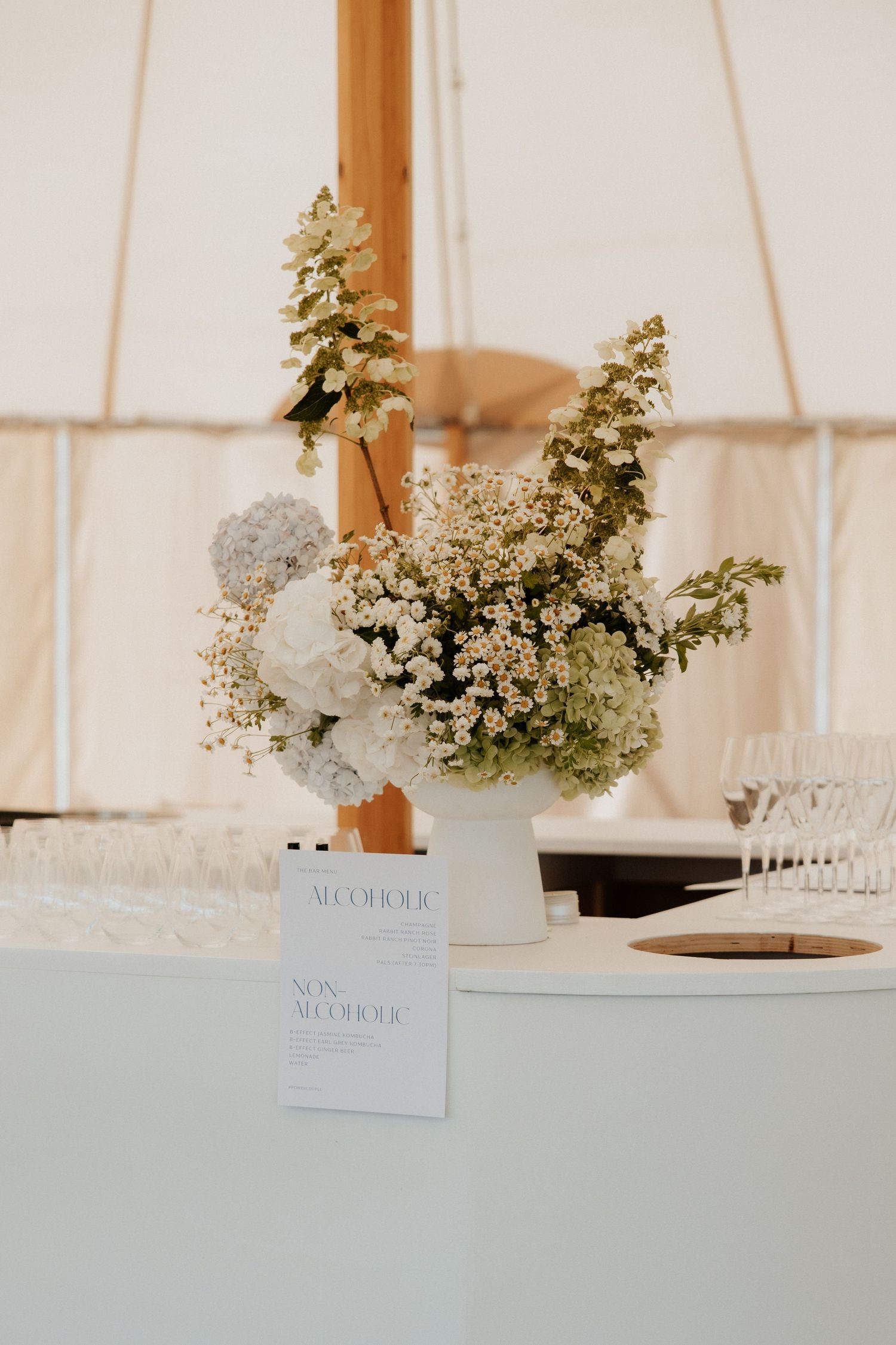 Elegant white floral centerpiece arrangement with greenery in a tent setting with menu card display.