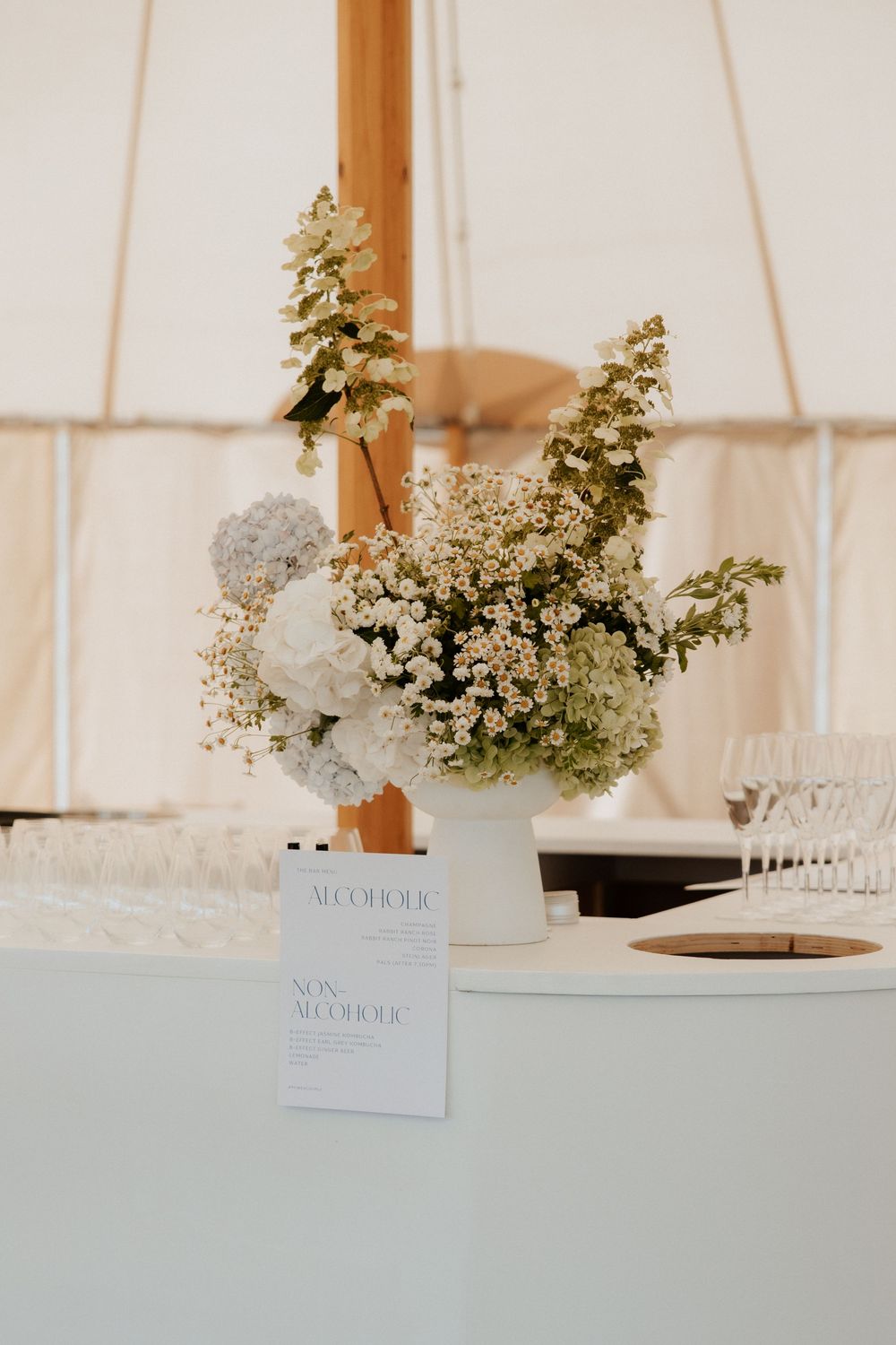 Elegant white floral centerpiece arrangement with greenery in a tent setting with menu card display.