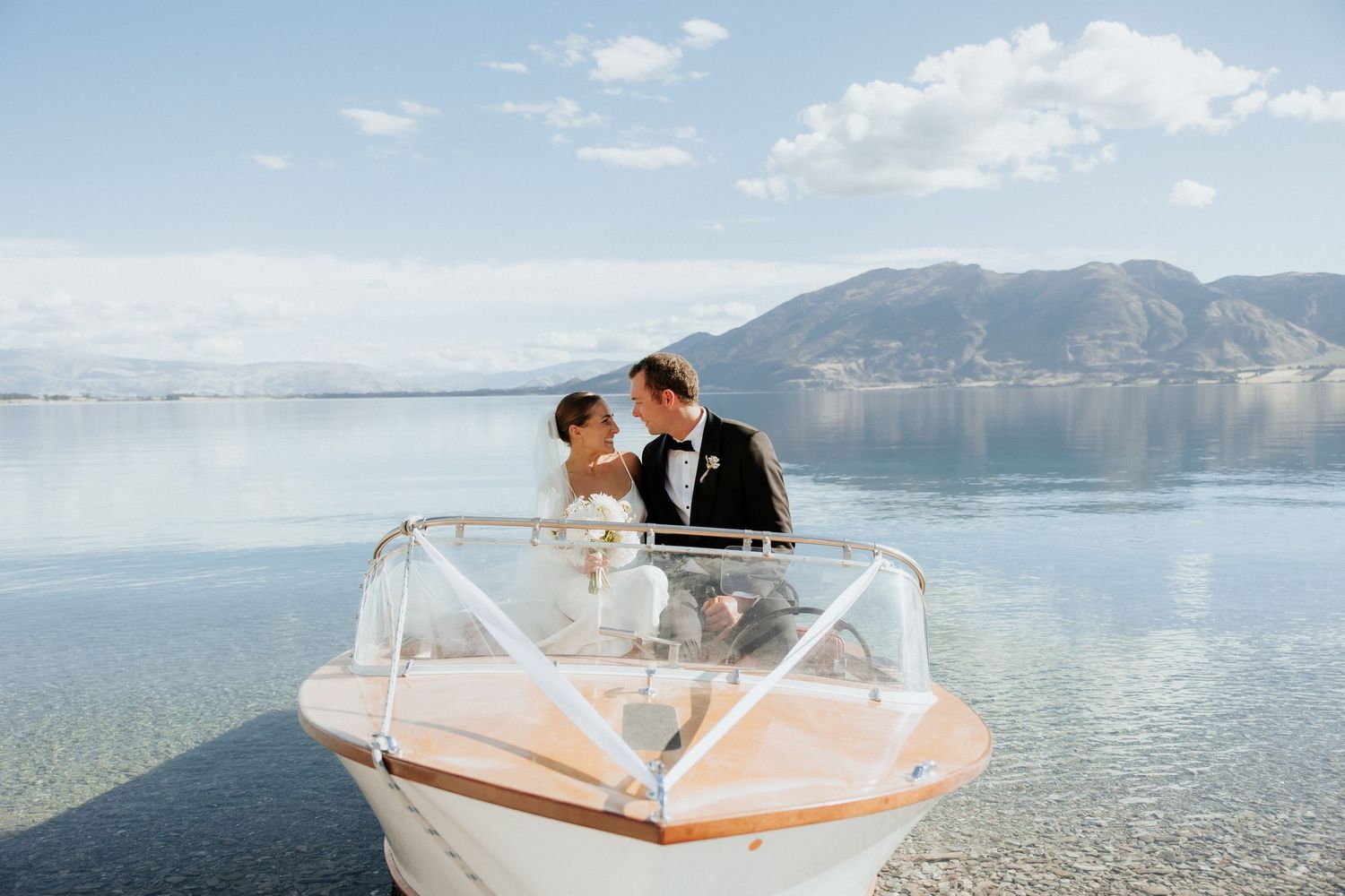 A couple sharing an intimate moment on a boat with mountain views across a serene lake.