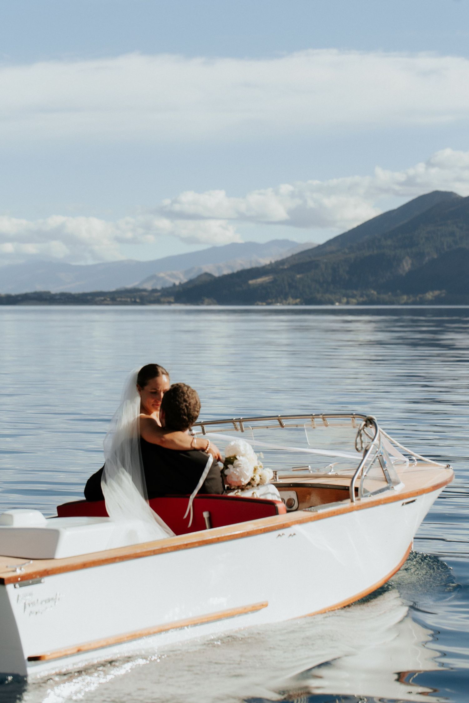 A couple enjoys a romantic boat ride on a serene mountain lake with snow-capped peaks in the background.