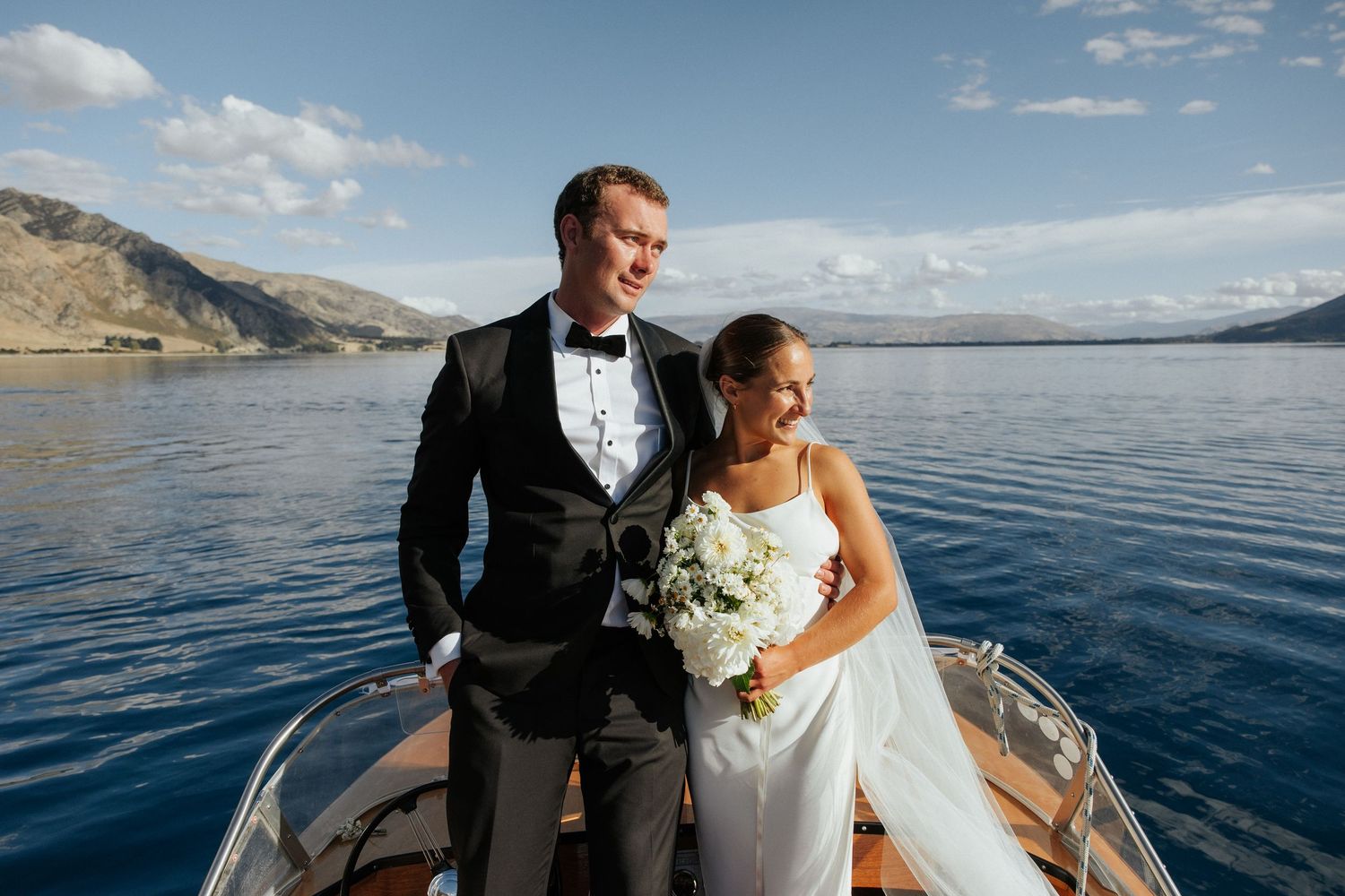 Newlywed couple posing together on a boat with scenic mountain lake views.