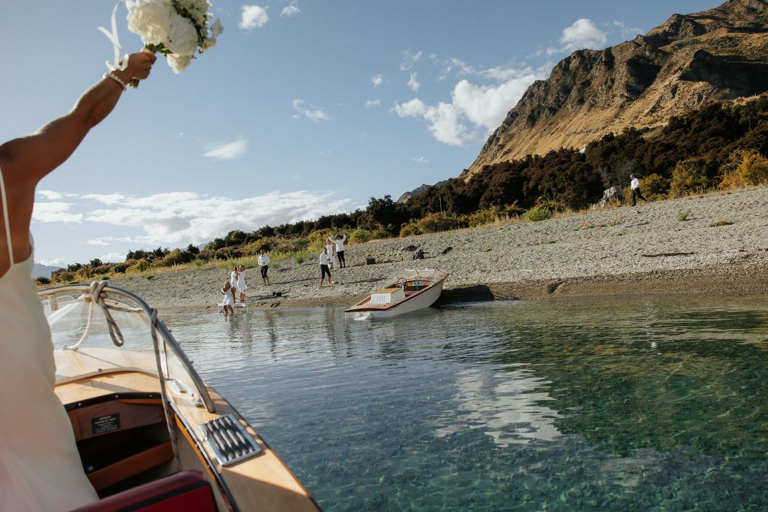 Wedding bouquet held up with mountain lake and boat in background.