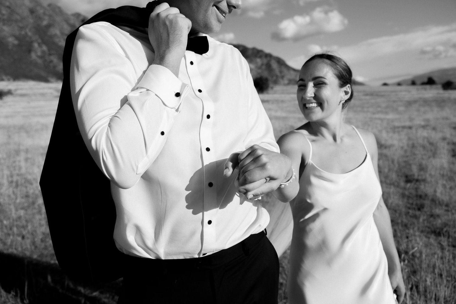A couple shares a joyful moment outdoors against a backdrop of rolling fields.