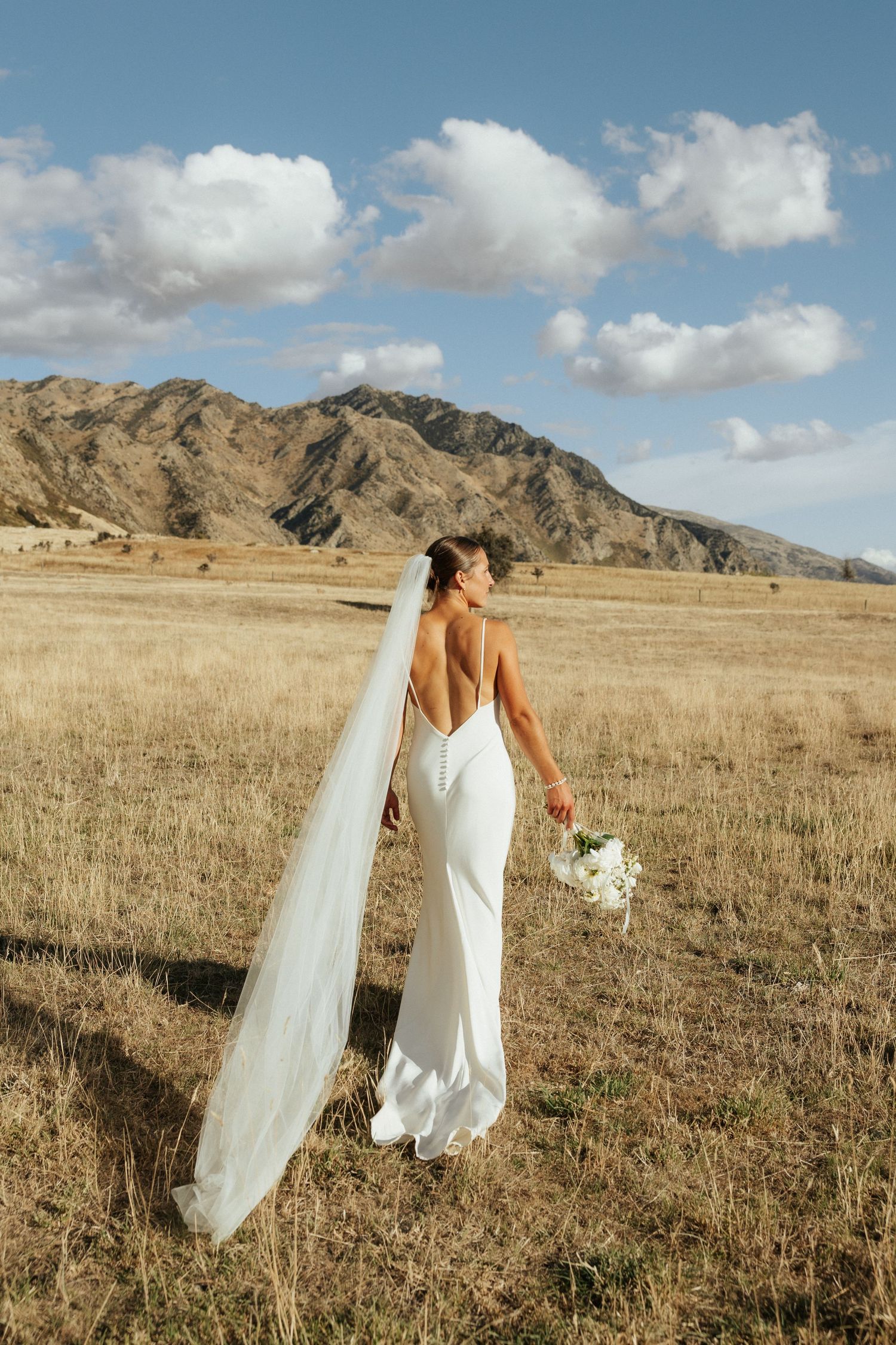 Wedding couple walking through golden grass field with mountains in the background.
