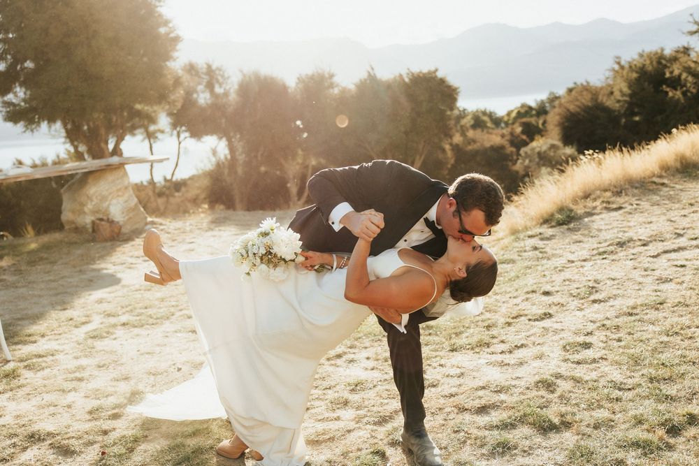 Romantic sunset dip kiss between newlyweds on mountainside with glowing backlight.